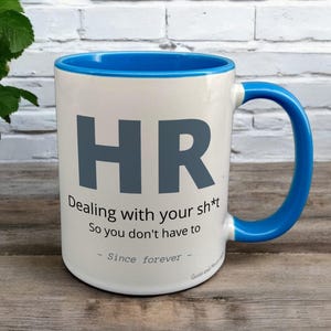 Blue & White Ceramic Mug with HR Design sat on a table. The Cup has a standard handle.