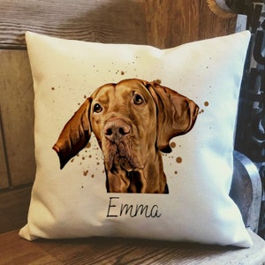 May include: Square cushion featuring a watercolour portrait of a brown dog, with the name "Emma" in script below the image. The cushion has brown paint splatter accents on a white background.