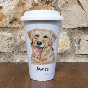 K&ouml;nnte beinhalten: Wei&szlig;e Keramik-Reisebecher mit einer Aquarell-Illustration eines Golden Retriever-Hundes. Der Becher tr&auml;gt eine schwarze Aufschrift mit dem Text "James" und "By Goose and Mouse".