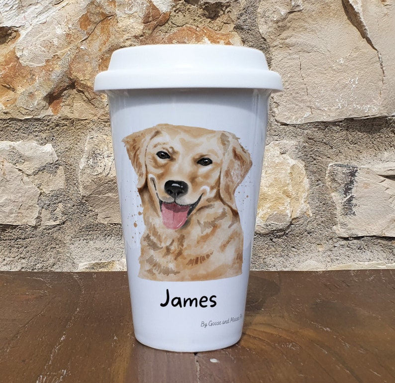 K&ouml;nnte beinhalten: Wei&szlig;e Keramik-Reisebecher mit einer Aquarell-Illustration eines Golden Retriever-Hundes. Der Becher tr&auml;gt eine schwarze Aufschrift mit dem Text "James" und "By Goose and Mouse".