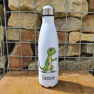 May include: White stainless steel water bottle with a green lizard graphic and the name "Jamie" printed on the bottom.
