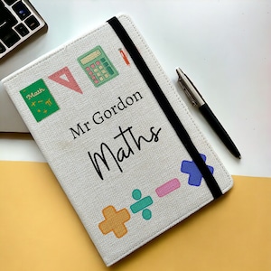 May include: White notebook with a black elastic closure. The cover features a calculator, protractor, pencil, and maths symbols. The text "Mr Gordon Maths" is printed on the cover.