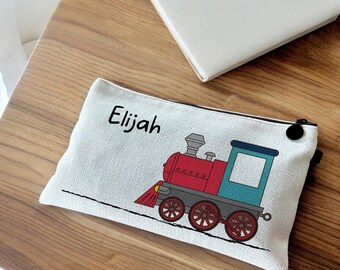May include: A white canvas zippered pouch with a red, blue, and gray cartoon train and the name "Elijah" printed on it.