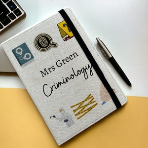 May include: A white notebook with a black elastic closure and a variety of crime-themed illustrations. The notebook is labelled "Mrs Green Criminology".