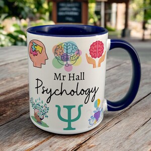 Navy & White Ceramic Mug with Psychology Design sat on a table. The Cup has a standard handle. Customisable text is printed below the Psychology design in a black text.