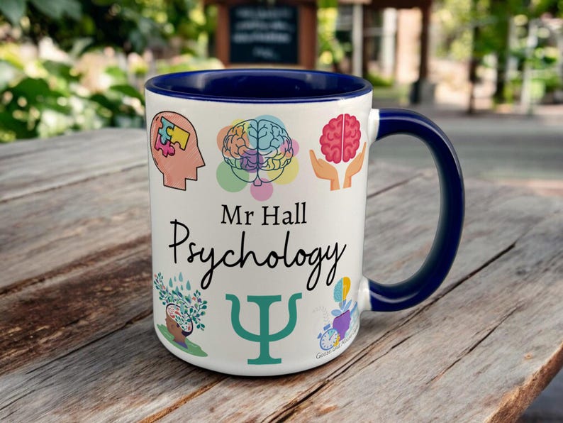Navy & White Ceramic Mug with Psychology Design sat on a table. The Cup has a standard handle. Customisable text is printed below the Psychology design in a black text.