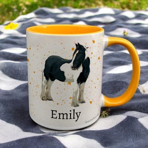 yellow & White Ceramic Mug with Horse Design sat on a table. The Cup has a standard handle. Customisable text is printed below the Horse design in a black text.