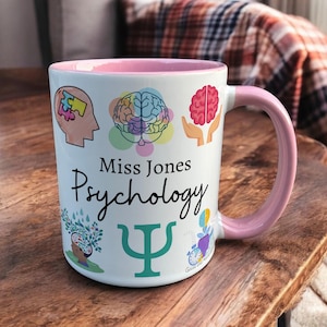 Pink & White Ceramic Mug with Psychology Design sat on a table. The Cup has a standard handle. Customisable text is printed below the Psychology design in a black text.