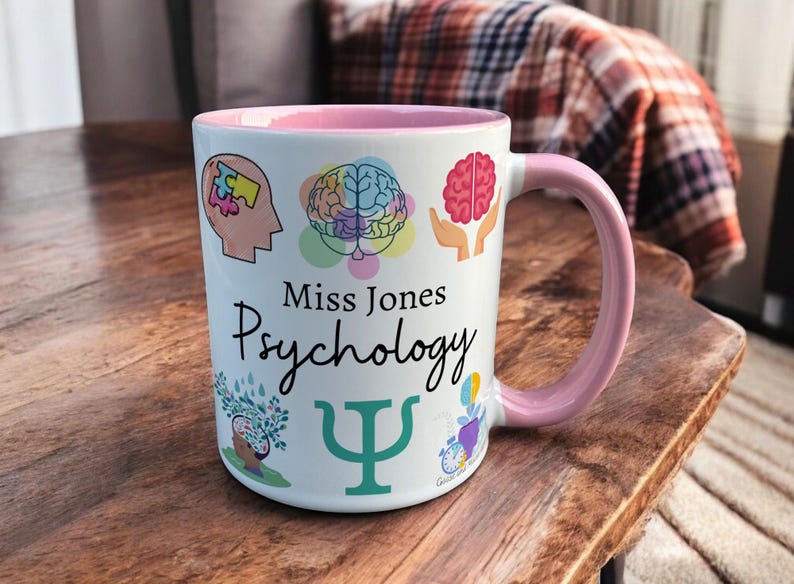 Pink & White Ceramic Mug with Psychology Design sat on a table. The Cup has a standard handle. Customisable text is printed below the Psychology design in a black text.