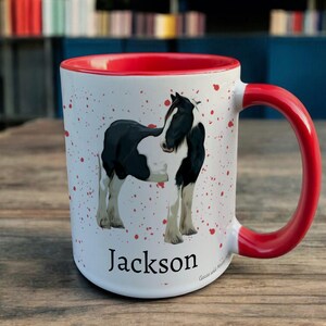Red & White Ceramic Mug with Horse Design sat on a table. The Cup has a standard handle. Customisable text is printed below the Horse design in a black text.