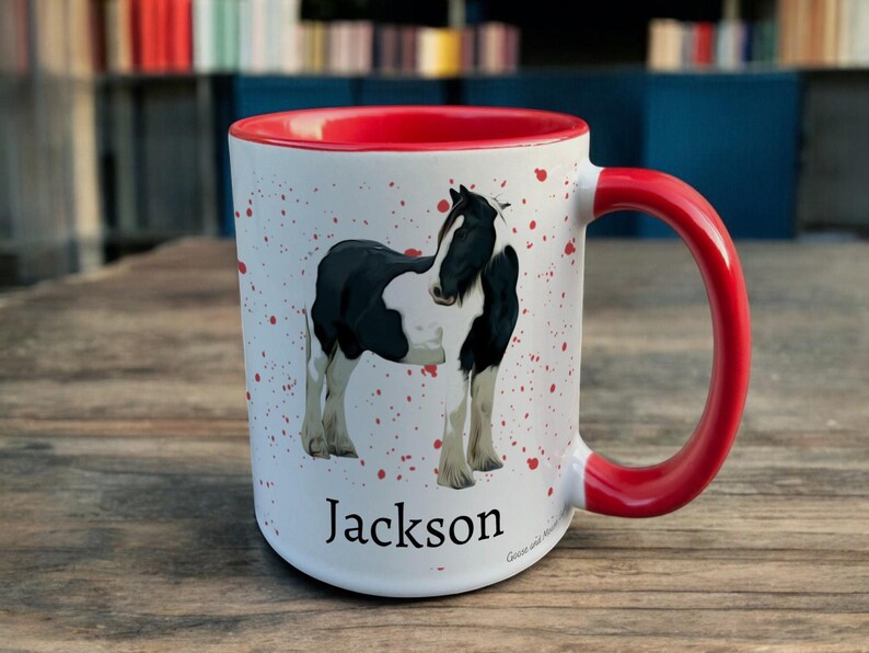 Red & White Ceramic Mug with Horse Design sat on a table. The Cup has a standard handle. Customisable text is printed below the Horse design in a black text.