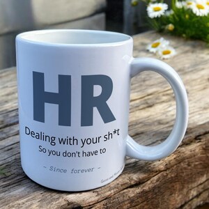 White Ceramic Mug with HR Design sat on a table. The Cup has a standard handle.