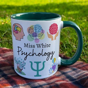 Green & White Ceramic Mug with Psychology Design sat on a table. The Cup has a standard handle. Customisable text is printed below the Psychology design in a black text.