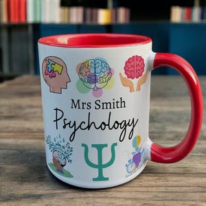 Red & White Ceramic Mug with Psychology Design sat on a table. The Cup has a standard handle. Customisable text is printed below the Psychology design in a black text.