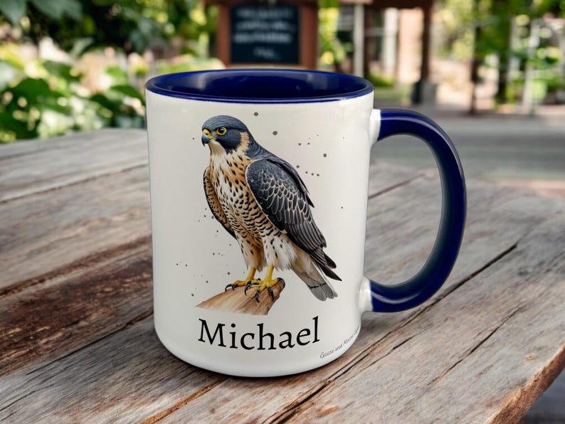 Navy & White Ceramic Mug with Falcon Design sat on a table. The Cup has a standard handle. Customisable text is printed below the Falcon design in a black text.