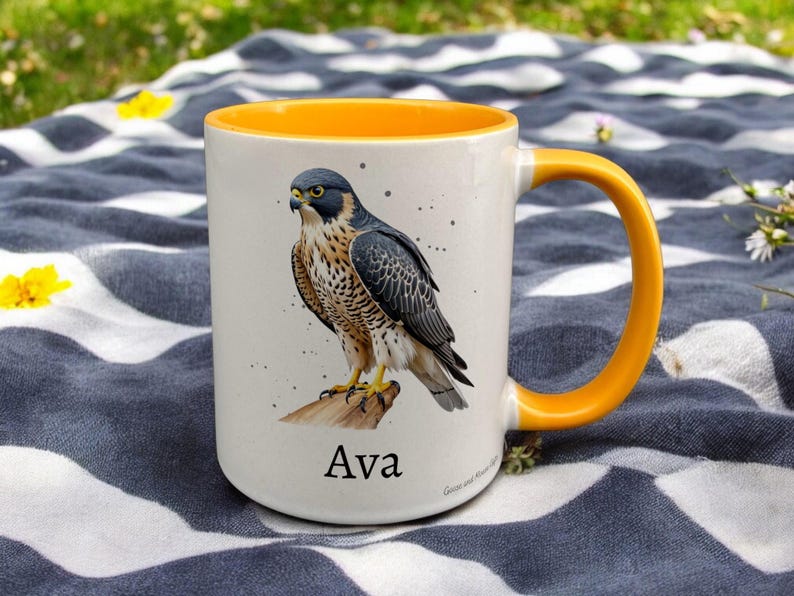 Yellow & White Ceramic Mug with Falcon Design sat on a table. The Cup has a standard handle. Customisable text is printed below the Falcon design in a black text.