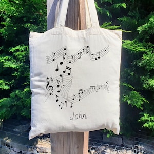 May include: A white canvas tote bag featuring a black musical note design and the name "John" printed on the front.