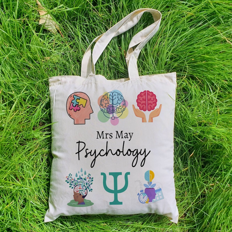 Puede incluir: Bolsa de tela blanca con un dise&ntilde;o colorido que presenta un cerebro, una pieza de rompecabezas, un &aacute;rbol, un s&iacute;mbolo de psicolog&iacute;a y un reloj. El texto "Mrs May Psychology" est&aacute; impreso en la bolsa.