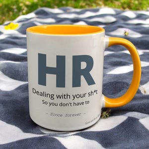 Yellow & White Ceramic Mug with HR Design sat on a table. The Cup has a standard handle.
