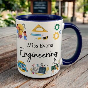 May include: White ceramic mug with a blue rim and handle. The mug features a colourful design of engineering-related icons and the text "Miss Evans Engineering".