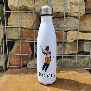 May include: White insulated water bottle featuring a graphic of a woman playing cricket and the name "Bethany" printed on the bottom.
