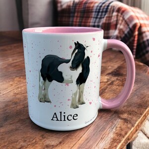 Pink & White Ceramic Mug with Horse Design sat on a table. The Cup has a standard handle. Customisable text is printed below the Horse design in a black text.
