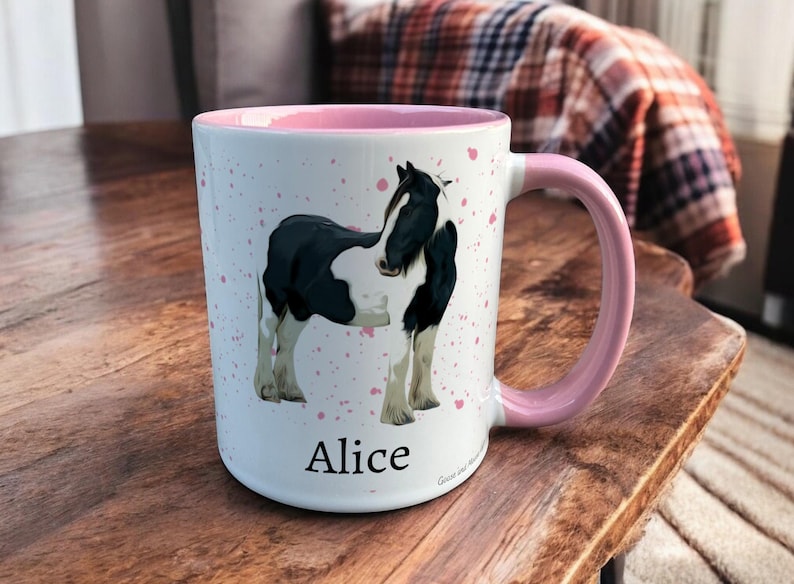 Pink & White Ceramic Mug with Horse Design sat on a table. The Cup has a standard handle. Customisable text is printed below the Horse design in a black text.