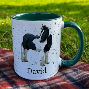 green & White Ceramic Mug with Horse Design sat on a table. The Cup has a standard handle. Customisable text is printed below the Horse design in a black text.