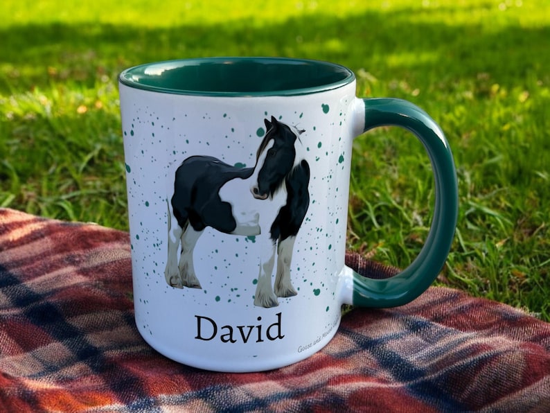 green & White Ceramic Mug with Horse Design sat on a table. The Cup has a standard handle. Customisable text is printed below the Horse design in a black text.