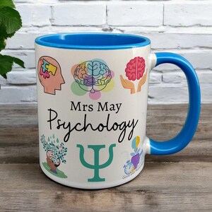 Blue & White Ceramic Mug with Psychology Design sat on a table. The Cup has a standard handle. Customisable text is printed below the Psychology design in a black text.