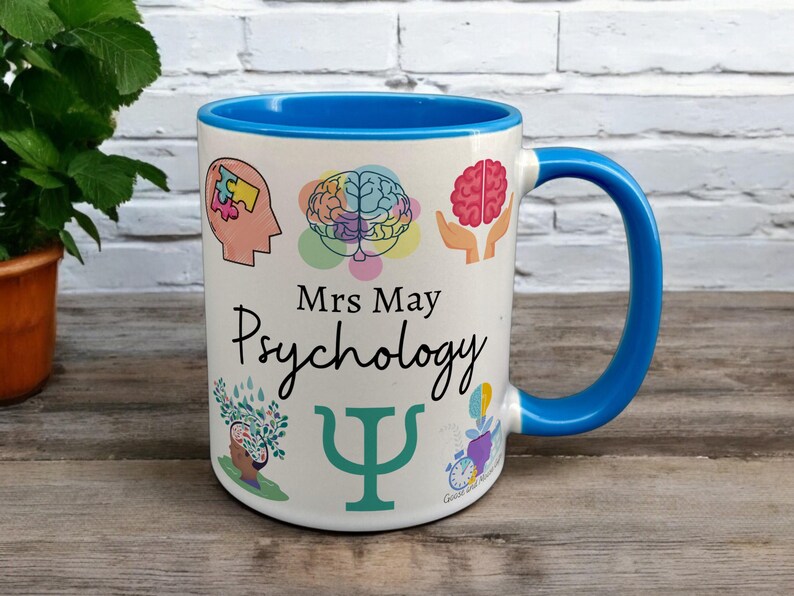 Blue & White Ceramic Mug with Psychology Design sat on a table. The Cup has a standard handle. Customisable text is printed below the Psychology design in a black text.