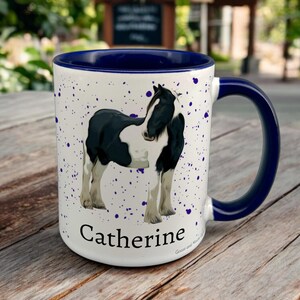 Navy & White Ceramic Mug with Horse Design sat on a table. The Cup has a standard handle. Customisable text is printed below the Horse design in a black text.