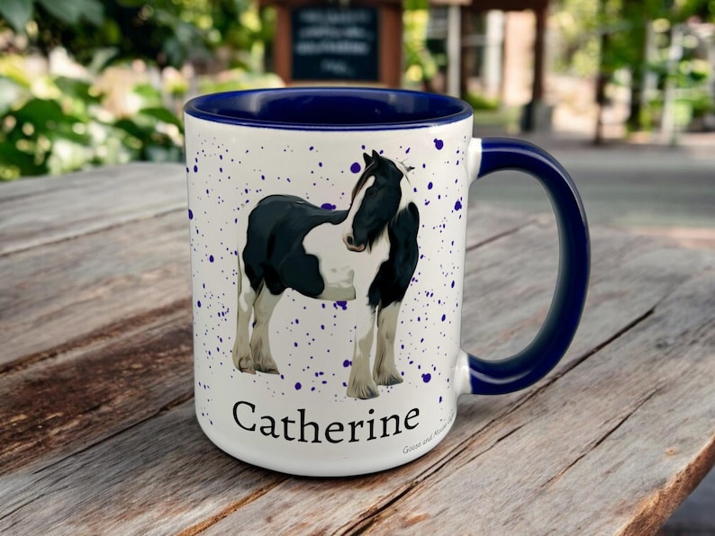 Navy & White Ceramic Mug with Horse Design sat on a table. The Cup has a standard handle. Customisable text is printed below the Horse design in a black text.