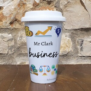 May include: White travel mug with a black and white design featuring the text "Mr Clark business" and various business-related icons. The mug has a black lid.