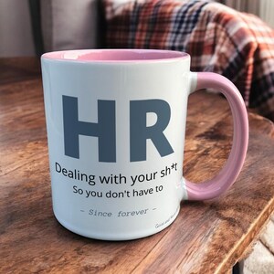 Pink & White Ceramic Mug with HR Design sat on a table. The Cup has a standard handle.