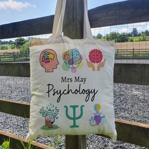 Puede incluir: Bolsa de tela blanca de lona con tem&aacute;tica de psicolog&iacute;a. Presenta un cerebro, una pieza de rompecabezas y una letra griega psi. El texto en la bolsa dice "Mrs. May Psychology".