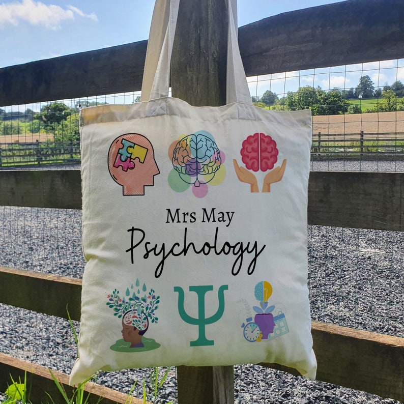 Puede incluir: Bolsa de tela blanca de lona con tem&aacute;tica de psicolog&iacute;a. Presenta un cerebro, una pieza de rompecabezas y una letra griega psi. El texto en la bolsa dice "Mrs. May Psychology".