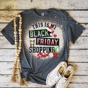May include: A gray t-shirt with a bleached design that says "This is my Black Friday Shopping Shirt". The design includes a coffee cup, a Christmas tree, a shopping cart, and a Santa hat.