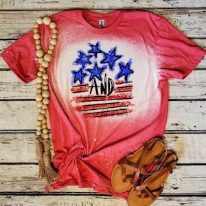 May include: Red, white, and blue bleached t-shirt with a graphic of stars and stripes and the word "AND" in black.