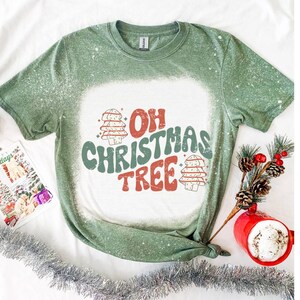 May include: Green t-shirt with a white bleach design that says "Oh Christmas Tree" with two stylized Christmas trees.