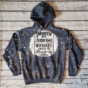 May include: Black hoodie with white bleach splatters and a white graphic that says "Smooth as Tennessee Whiskey Sweet as Strawberry Wine".