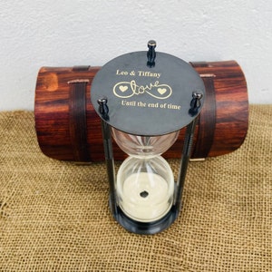 May include: A black hourglass with a brass top engraved with "Leo & Tiffany" and "Love Until the end of time" with two hearts. The hourglass is in a wooden box.