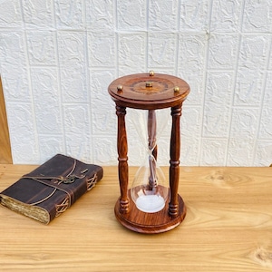 Puede incluir: Un reloj de arena de madera con un bulbo de vidrio y una cita grabada en la parte superior: "Hasta el fin del tiempo, estaremos juntos".