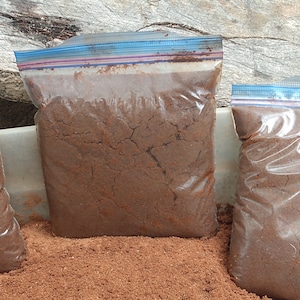 May include: Three clear plastic bags filled with a brown, granular substance. The bags are sealed with a zipper closure and have a blue and white striped design.