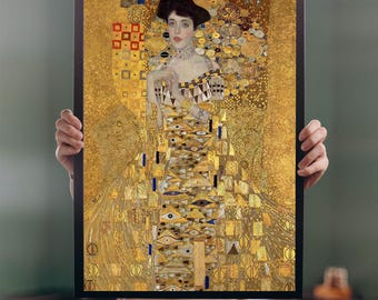 May include: Framed print of a Gustav Klimt painting, featuring a woman in an ornate gold dress with intricate patterns. The artwork has a gold background with geometric and organic shapes, and the woman has a dark hat and a delicate expression.