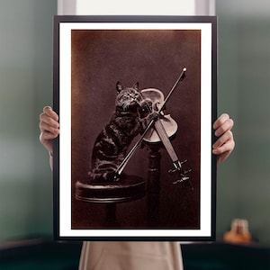 May include: Sepia-toned framed print featuring a cat playing a violin. The cat, with dark tabby markings, is seated on a small stool, holding the bow and violin. The image has a vintage aesthetic, with a dark background and a black frame.