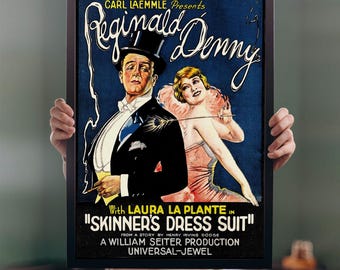 May include: A framed vintage movie poster for "Skinner's Dress Suit" featuring Reginald Denny and Laura La Plante. The poster has a dark blue background with the movie title and credits in white and yellow. The actors are depicted in formal attire.