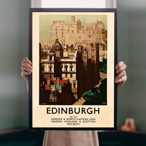 Op de afbeelding: Een ingelijste vintage reisprent voor Edinburgh, Schotland, met een gedetailleerde illustratie van de architectuur van de stad. De poster heeft een beige achtergrond en het woord "Edinburgh" in vette letters. De poster is zwart omlijst.