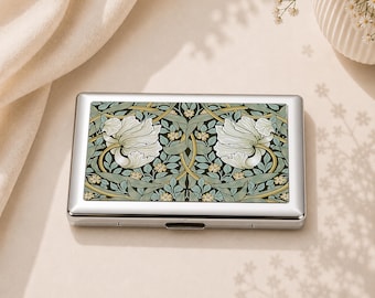 May include: A rectangular metal case with a polished silver finish and a hinged lid. The top surface features a decorative print of white flowers, green leaves, and winding vines arranged in a symmetrical, repeating botanical pattern.