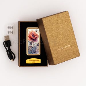 May include: A gold-framed lighter with a watercolor floral design featuring red and purple flowers. The lighter is in a black box with a gold-colored lid. The box has the word "LIGHTER" printed on it. A USB charging cable and spare parts are included.
